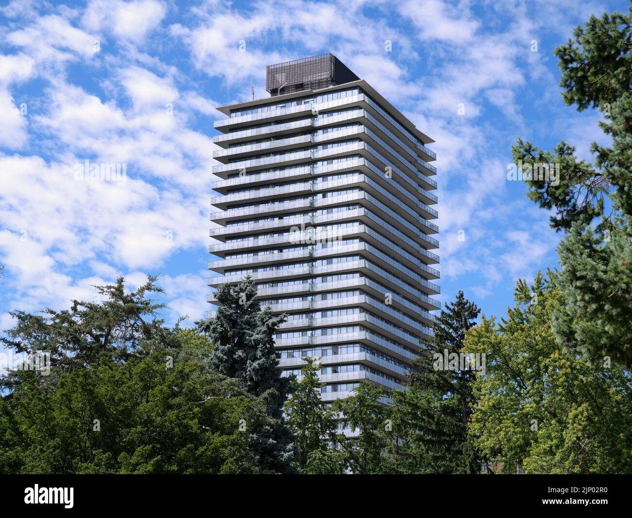 Tall modern apartment building with balconies, surrounded by trees Stock Photo