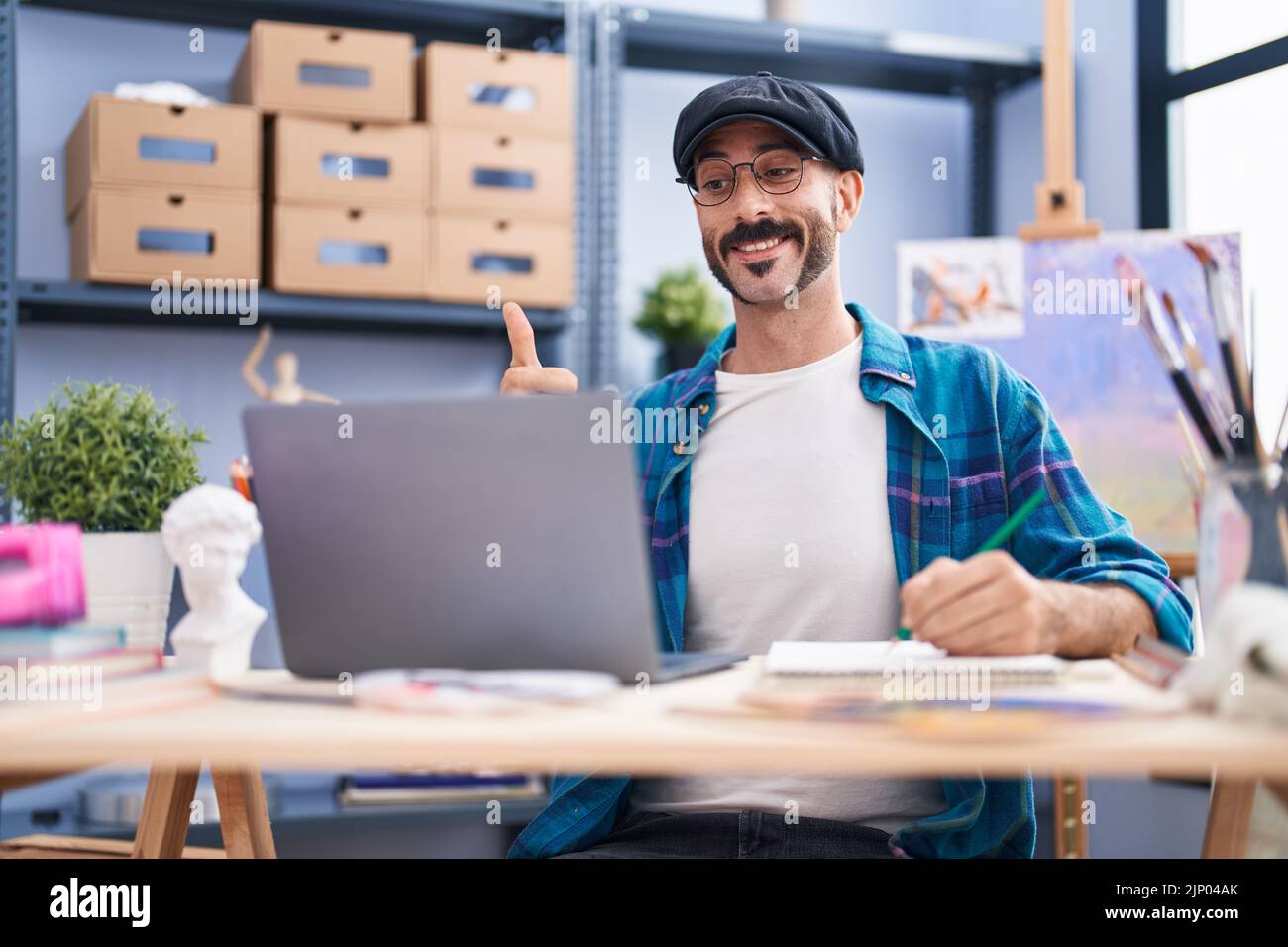 Hispanic man with beard doing online video call at art studio smiling