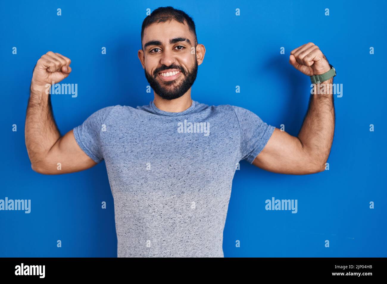 Middle east man with beard standing over blue background showing arms muscles smiling proud. fitness concept. Stock Photo