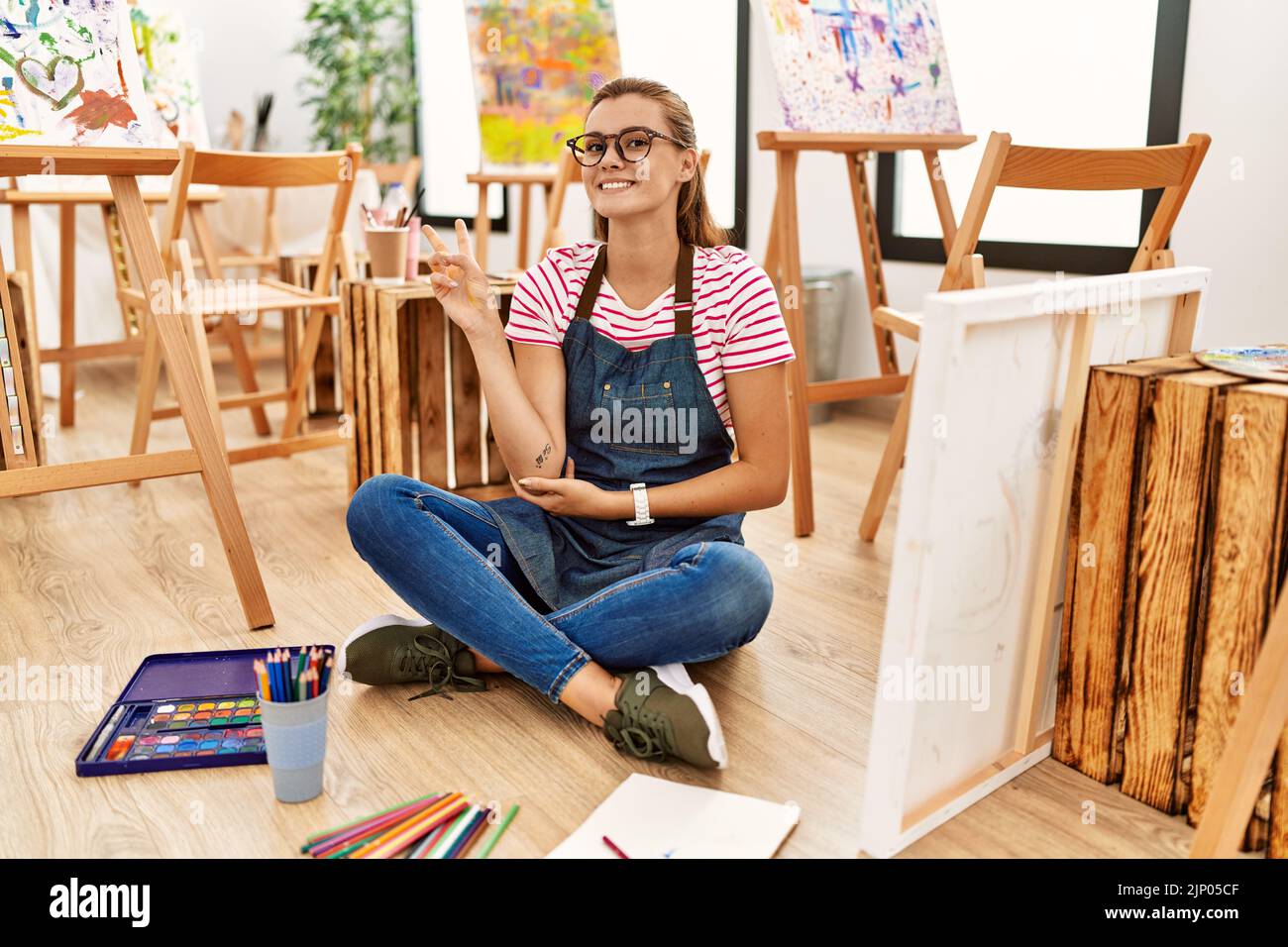 Young brunette woman at art studio sitting on the floor smiling with ...