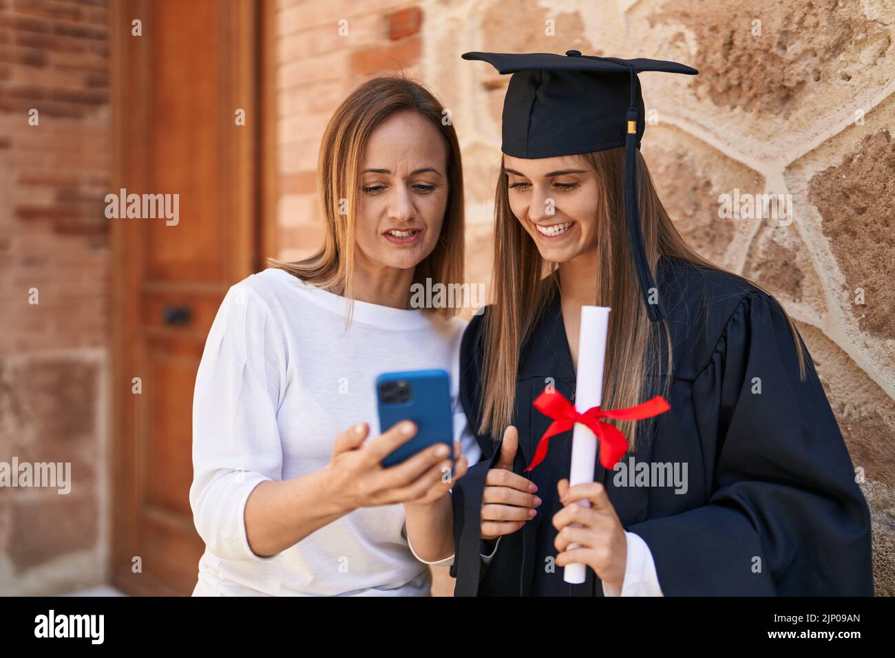 Two women mother and graduated daughter using smartphone at campus ...