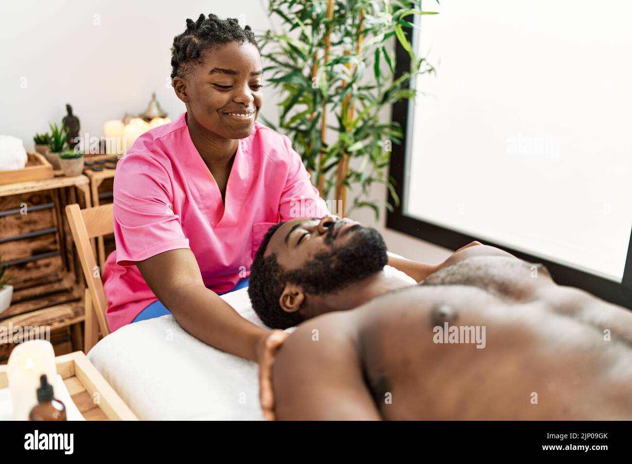 Young physiotherapist woman giving head massage to african american man at the clinic. Stock Photo