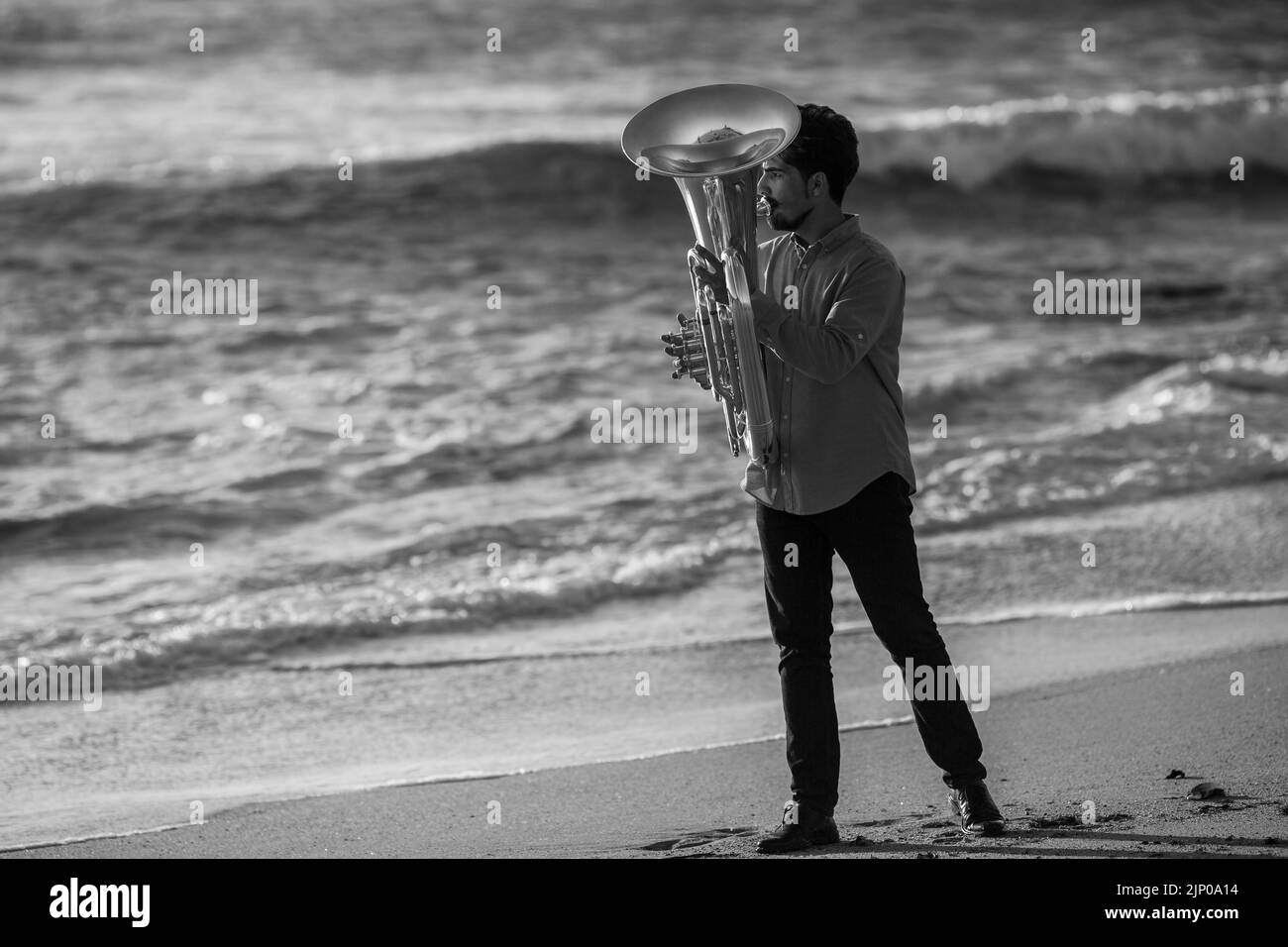 A man musician playing a tuba on the ocean beach. Black and white photo. Stock Photo