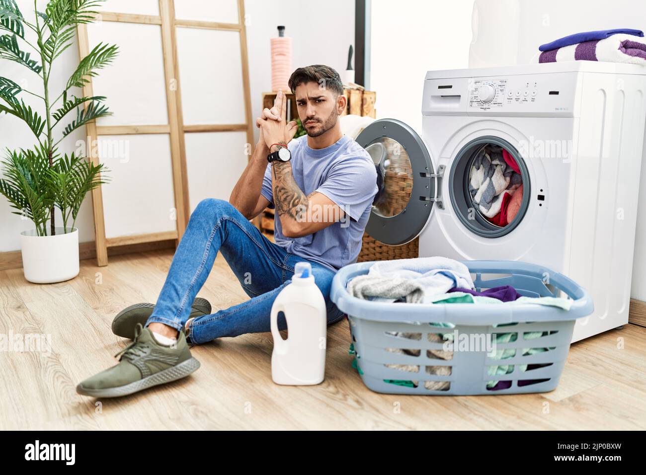 Young hispanic man putting dirty laundry into washing machine holding