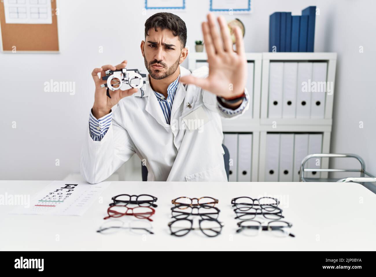 Terminate Spectacles Young optician man holding optometry glasses doing stop sing with palm ...