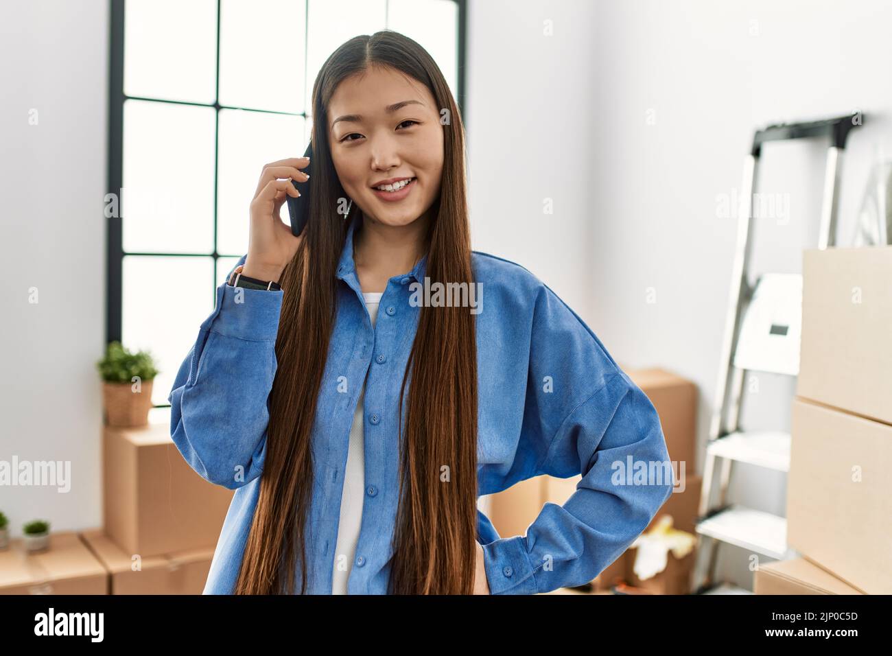 Young chinese girl smiling happy talking on the smartphone at new home ...