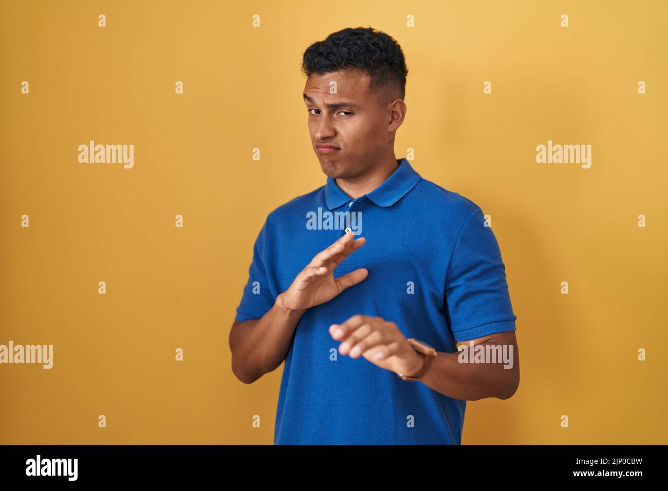 Young hispanic man standing over yellow background disgusted expression ...