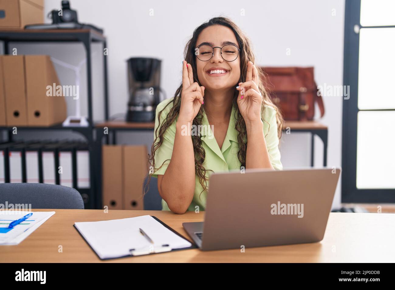 Young hispanic woman working at the office wearing glasses gesturing ...