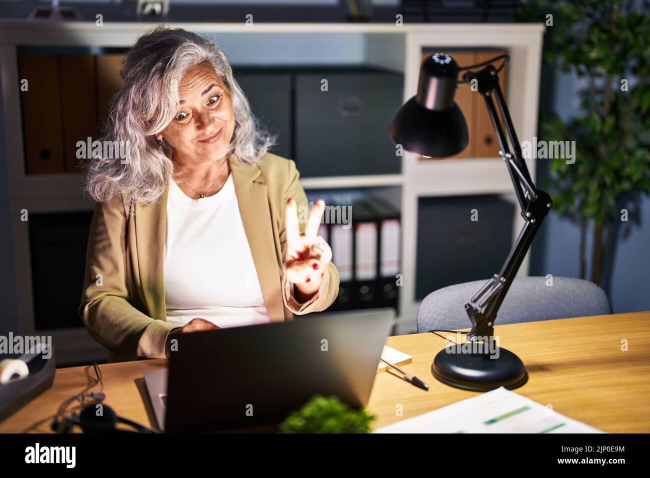 Middle age woman with grey hair working using computer laptop late at ...