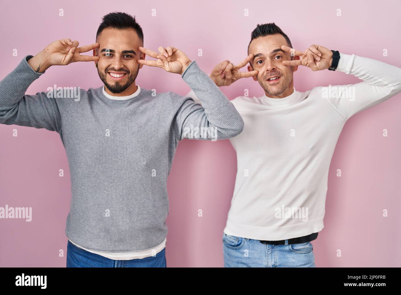 Homosexual couple standing over pink background doing peace symbol with ...