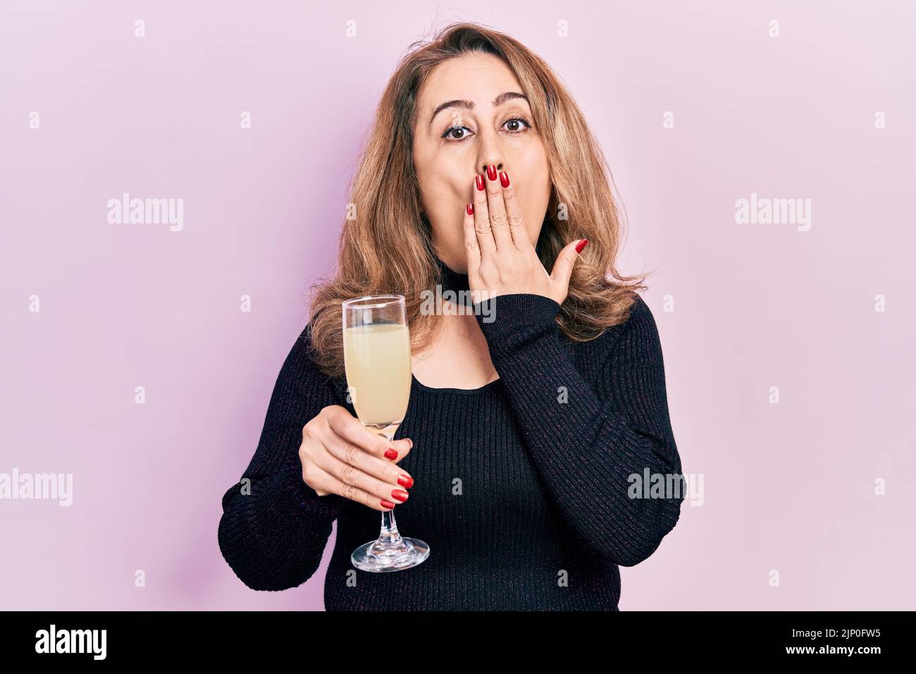 Middle age caucasian woman drinking glass of champagne covering mouth with hand, shocked and afraid for mistake. surprised expression Stock Photo