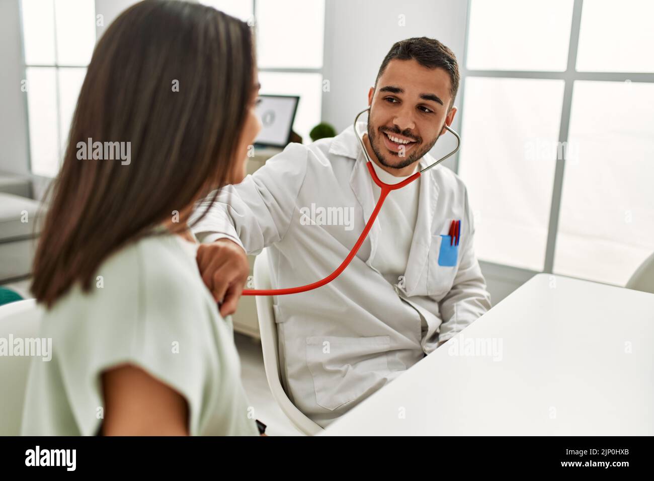 Doctor auscultating latin woman using stethoscope at clinic Stock Photo ...