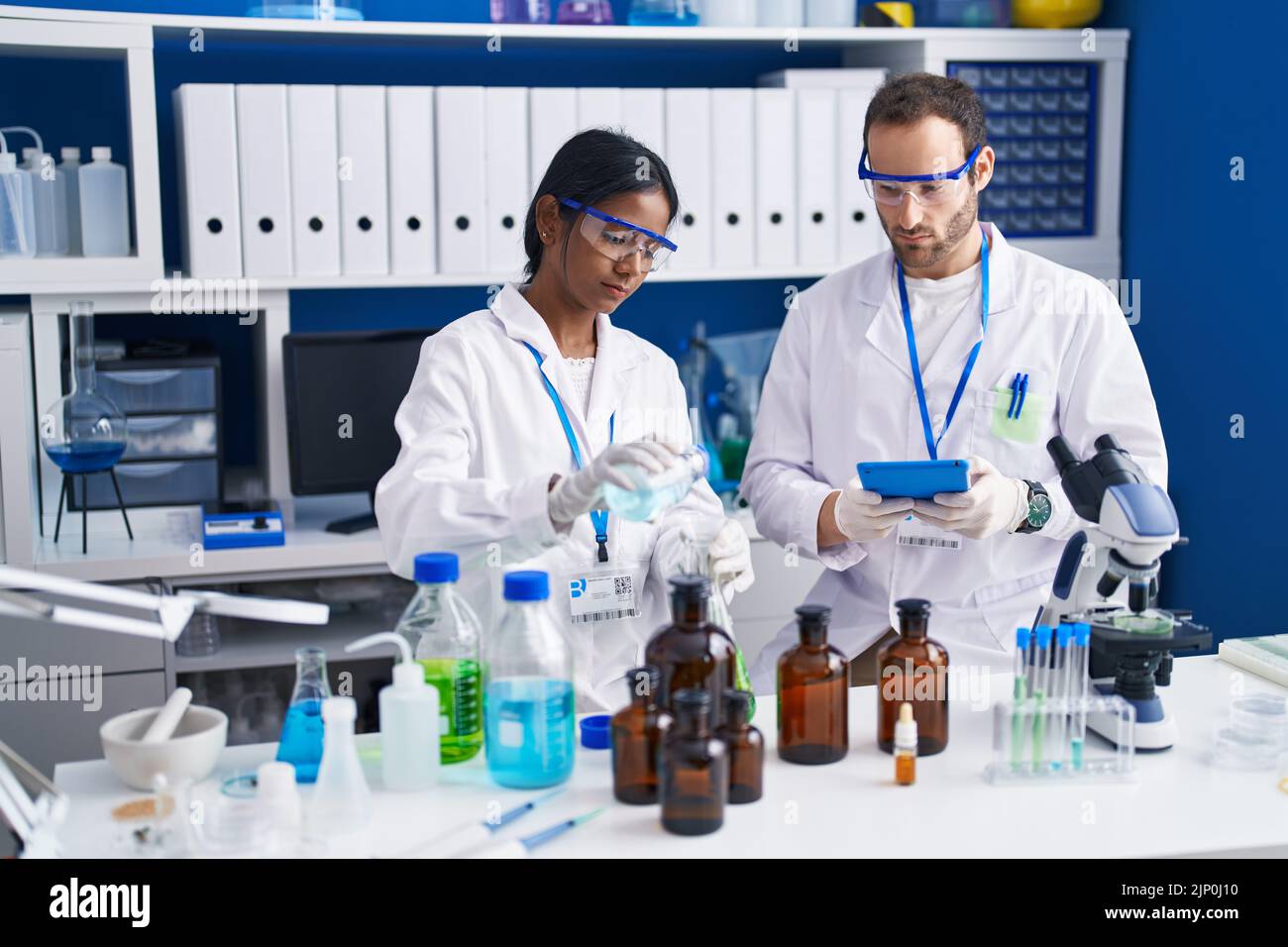 Man and woman scientists using touchpad measuring liquid at laboratory ...