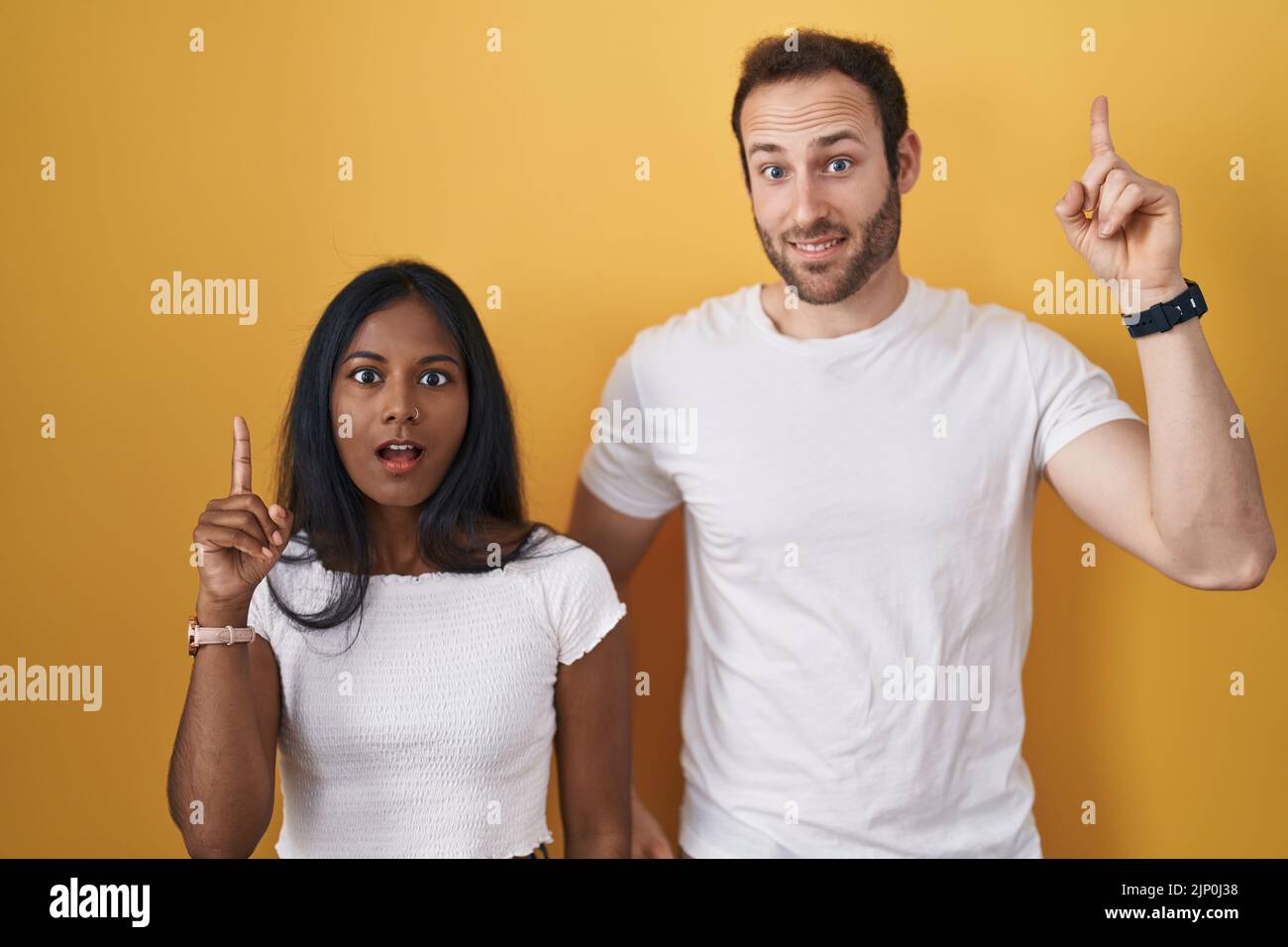 Interracial couple standing over yellow background pointing finger up with successful idea. exited and happy. number one. Stock Photo