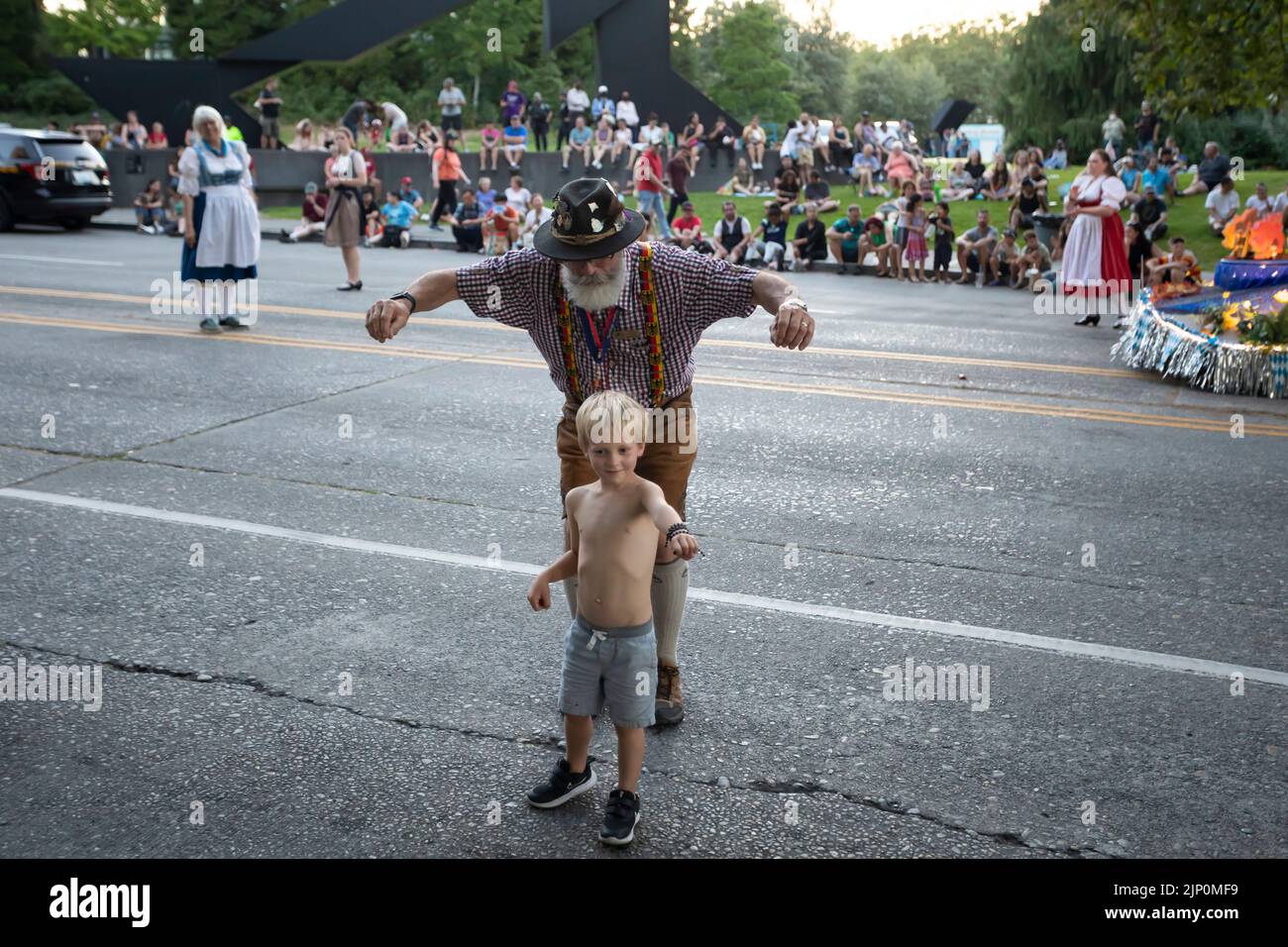 A participant in lederhosen sneaks up on a young spectator during the Seafair Torchlight Parade in Seattle on Saturday, July 30, 2022. Stock Photo
