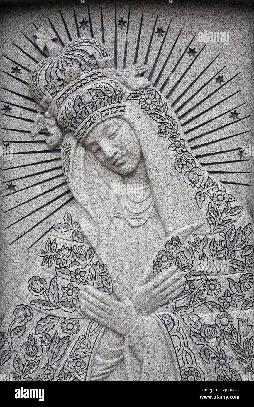 Religious female figure depicted on grey granite memorial monument in a