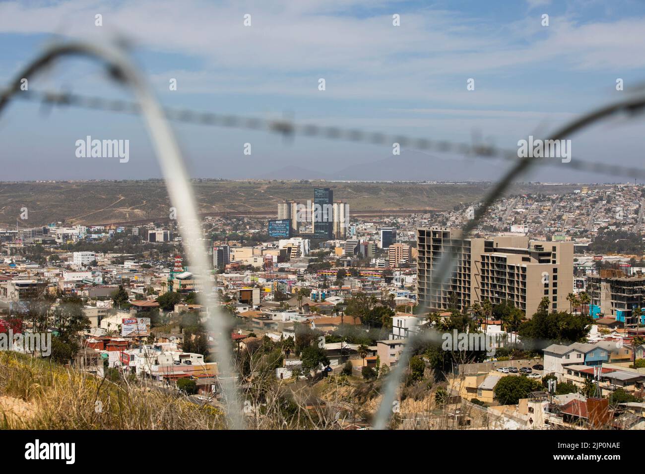 Tijuana, Baja California, Mexico - September 11, 2021: Barbed and razor wire frames a daytime view of the downtown skyline of Tijuana. Stock Photo