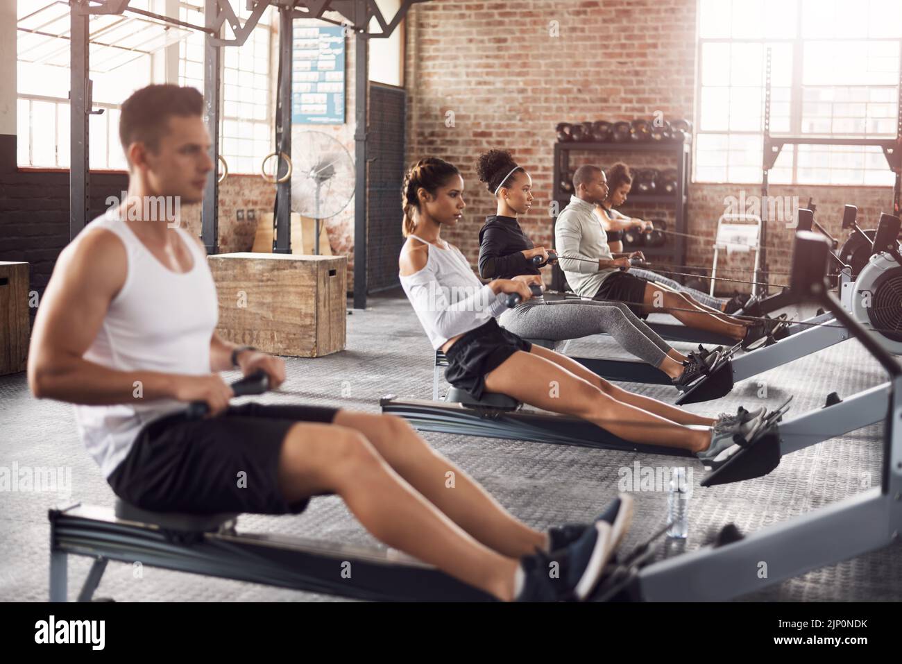 For a full body workout try the rowing machine. a young woman working out with a rowing machine in the gym. Stock Photo