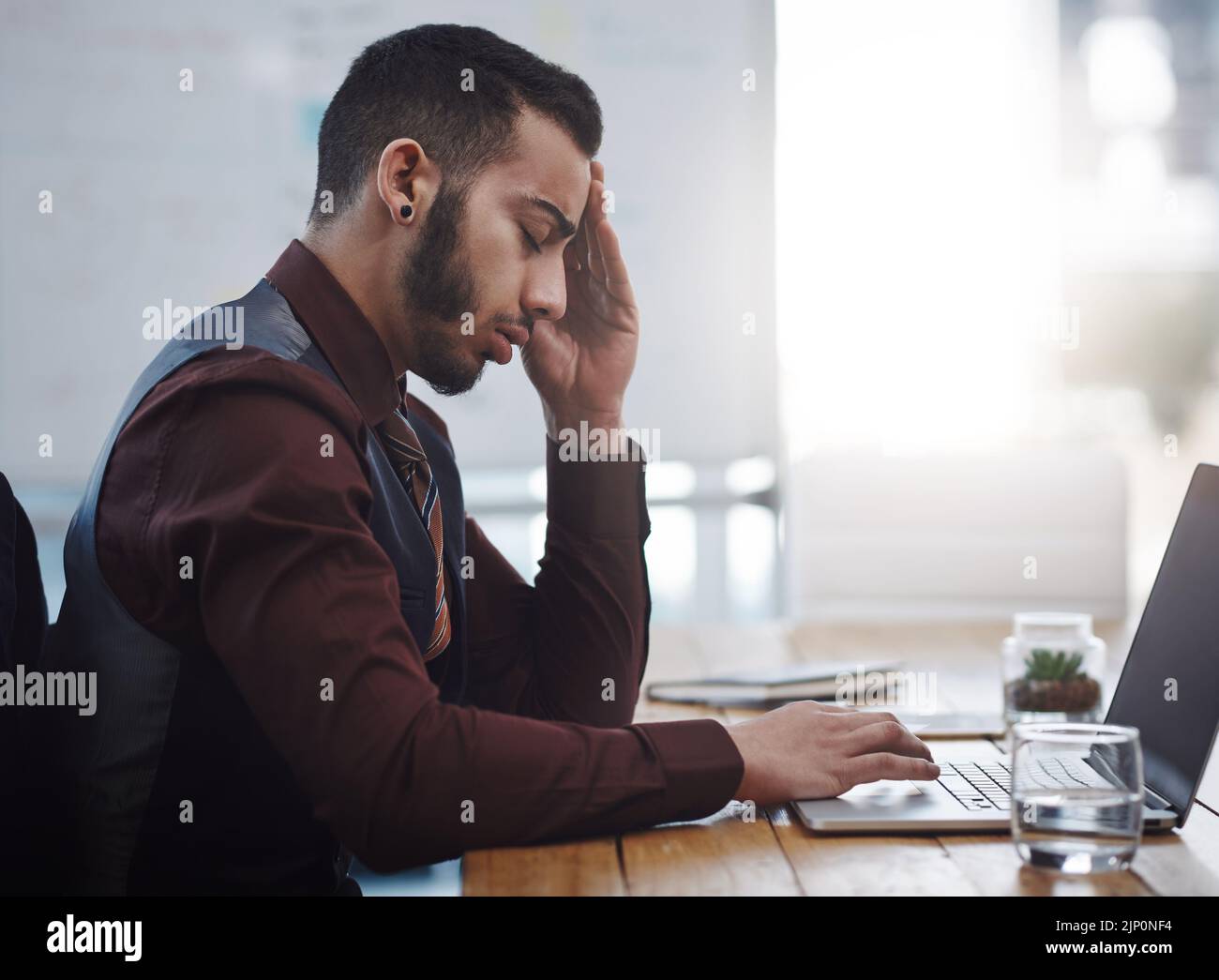 This headache is just the most frustrating. a young businessman looking stressed out while working in an office. Stock Photo