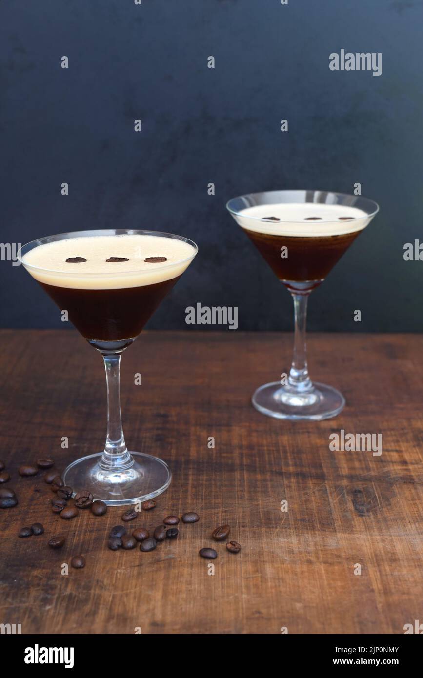 Glasses of espresso martini with coffee beans on wooden table and black