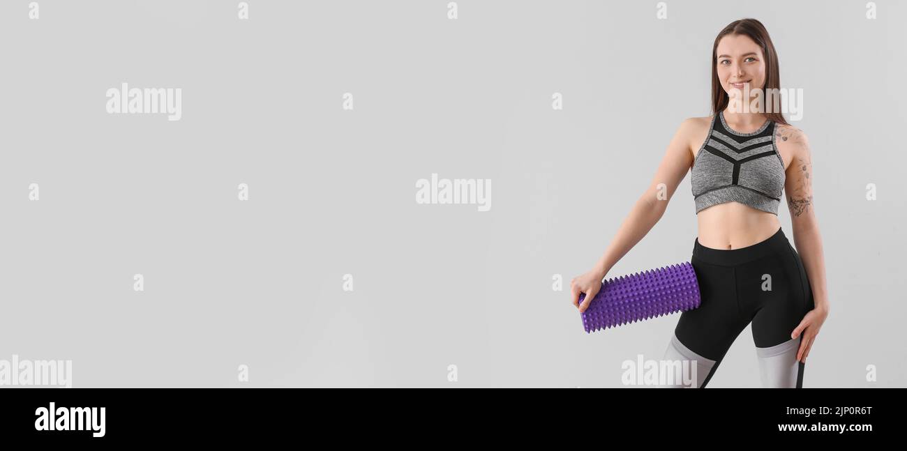 Sporty woman holding foam roller on grey background with space for text ...
