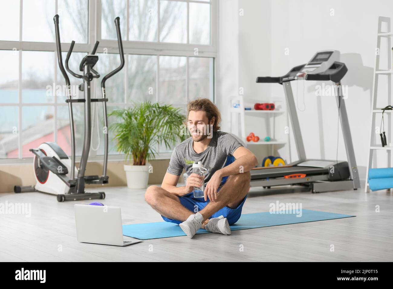Sporty young man with laptop and bottle of water in gym Stock Photo - Alamy