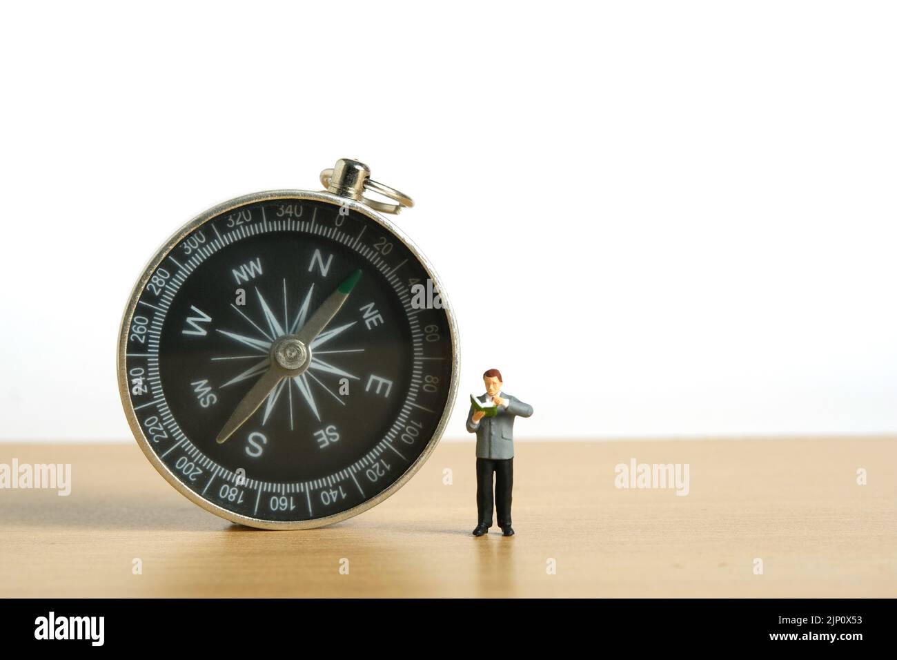 Miniature people toy figure photography. A men stand beside compass while reading a book. Image photo Stock Photo