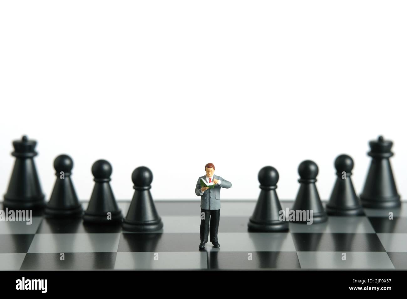 Miniature people toy figure photography. A men student standing above chessboard with pawn and knight, isolated on white background. Image photo Stock Photo