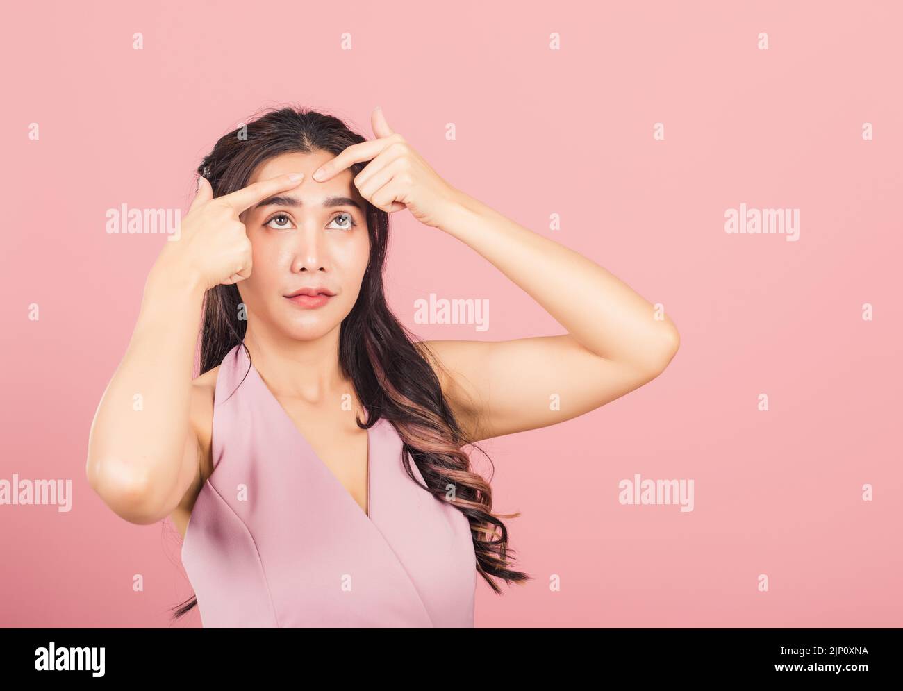 Portrait teenage Asian beautiful young woman having skin problems squeezing pimples on her face, studio shot on pink background, with copy space, Thai Stock Photo