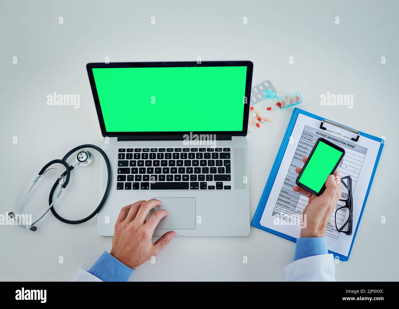 Technology helps keep track of it all. High angle shot of an unrecognizable doctor using a laptop and cellphone with a green screen in his office. Stock Photo