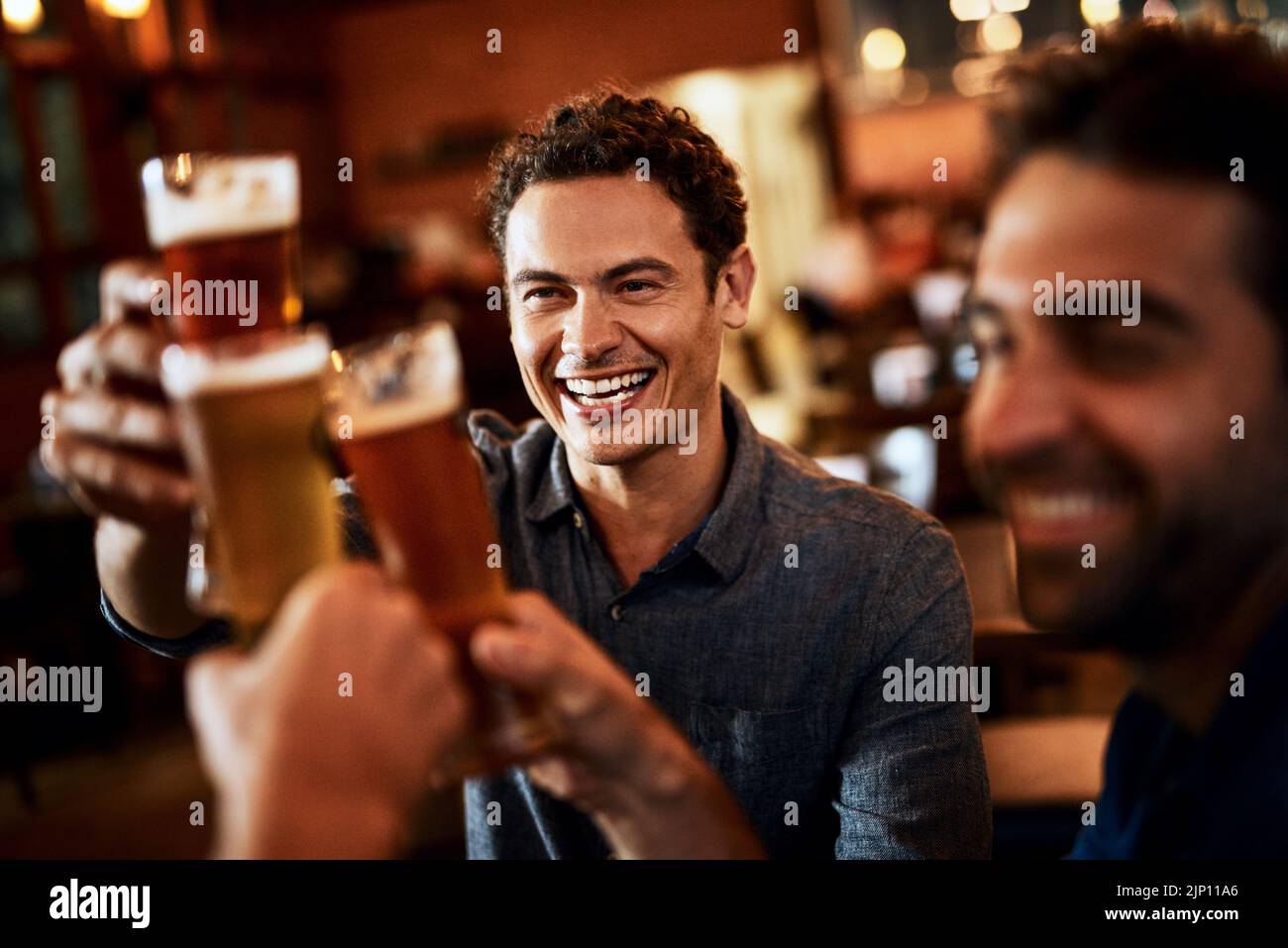 Whos buying the next set of beers. a group of young friends seated at a table together while enjoying a beer and celebrating with a celebratory toast Stock Photo