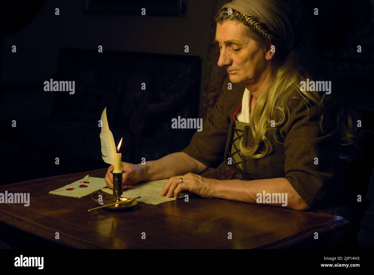 Woman in peasant historical costume writing a letter with a feather quill Stock Photo