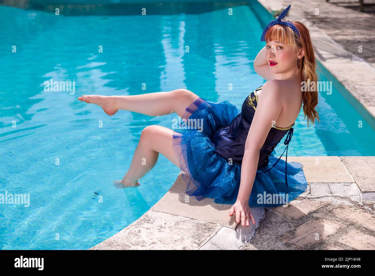 Attractive young woman dressed in a sexy sailor costume as a pinup girl on the edge of a swimming pool Stock Photo