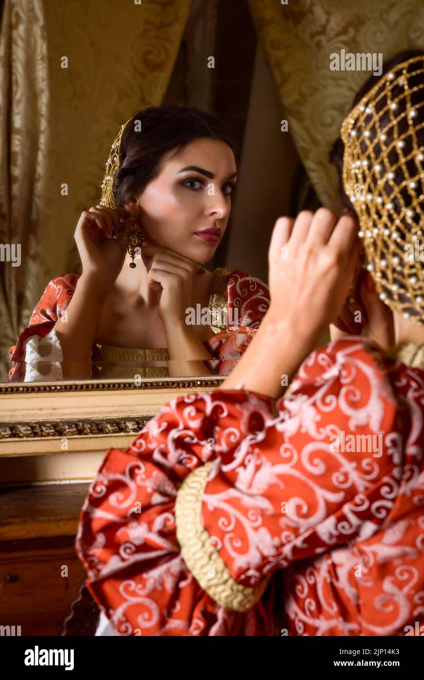 Beautiful woman in renaissance gown looking into an antique golden mirror in her castle Stock Photo