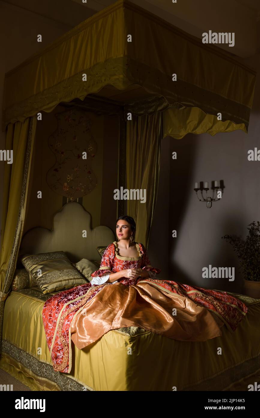 Golden medieval bedroom with beautiful canopy bed.  A lady in renaissance dress is sitting on the bed. Stock Photo