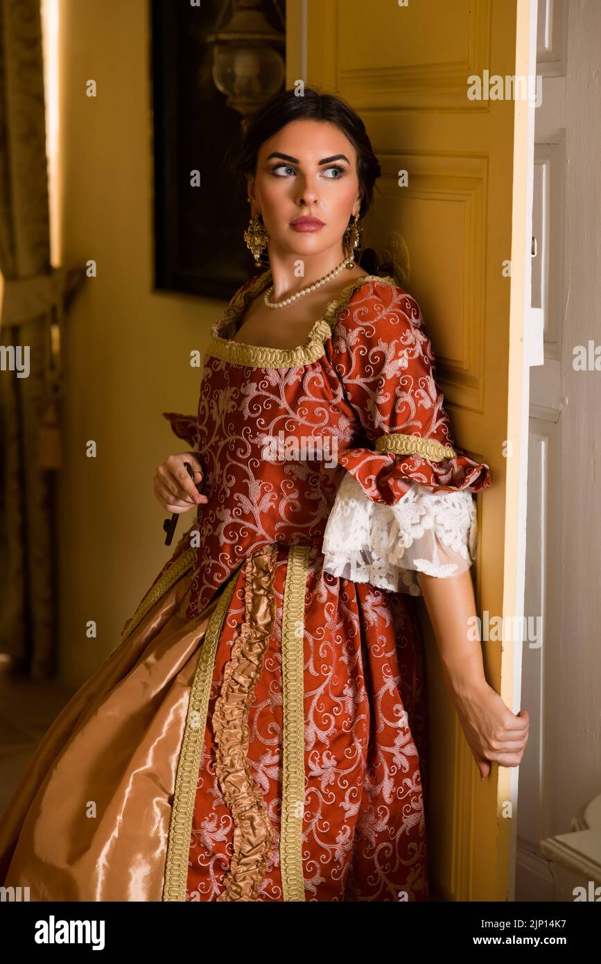 Beautiful woman in late renaissance costume posing between the open doors of a medieval castle. Stock Photo