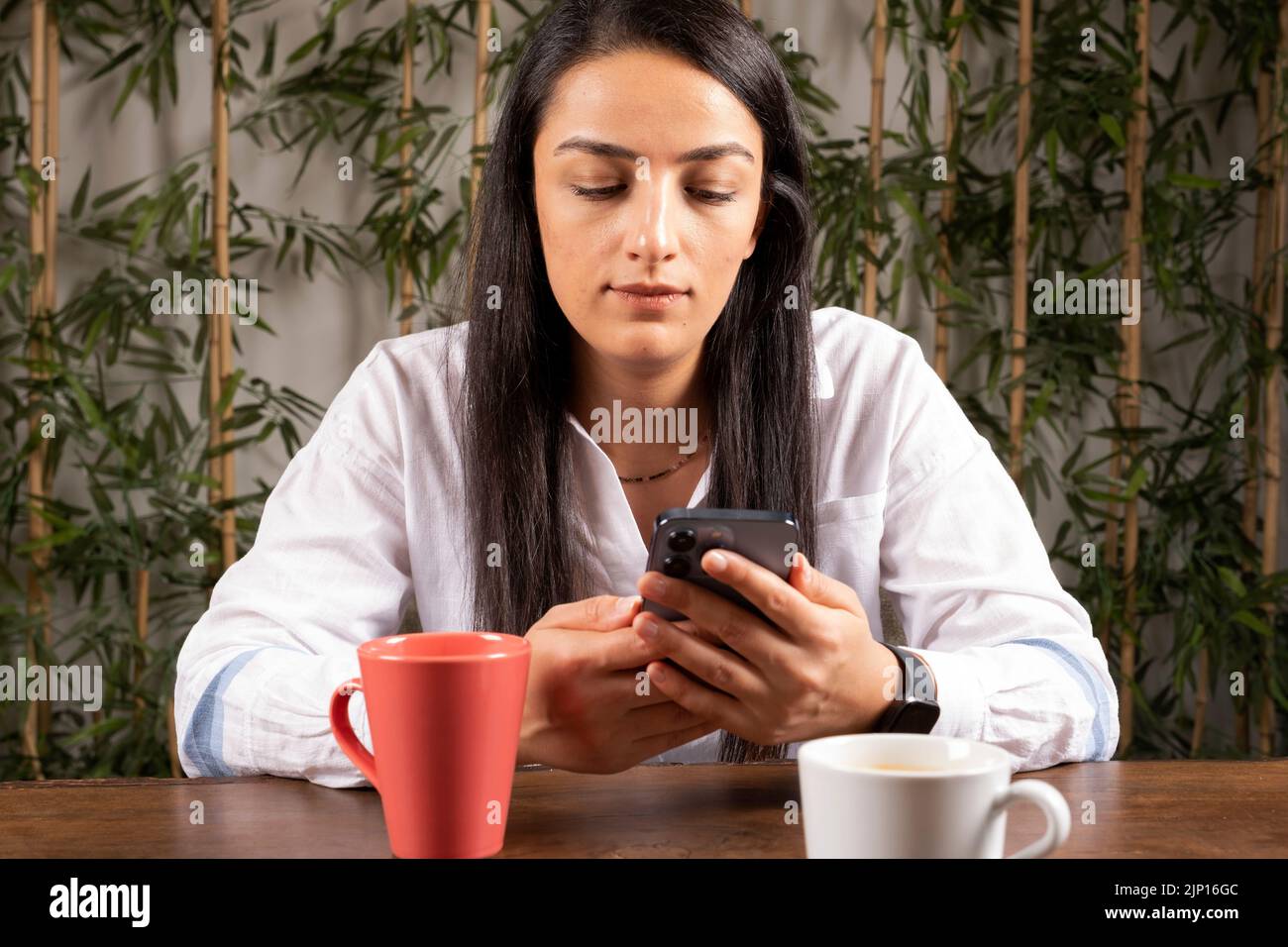 Using smartphone, front view portrait of young woman sitting at cafe and using smartphone. Little bored face expression, looking social media. Stock Photo