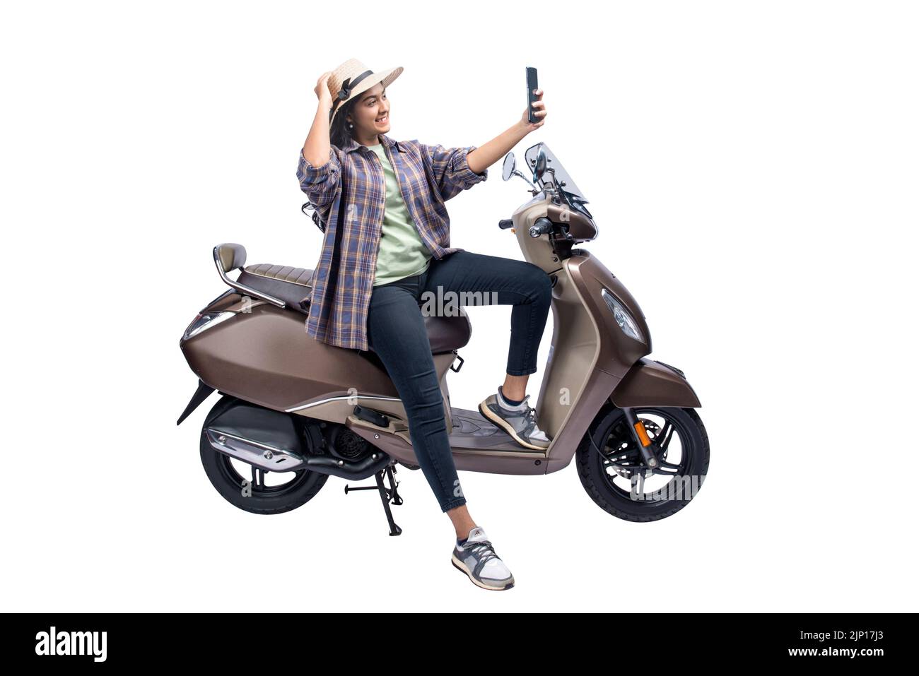 An Asian woman with a hat is sitting on a scooter and taking a self-portrait with a mobile phone isolated over white background Stock Photo