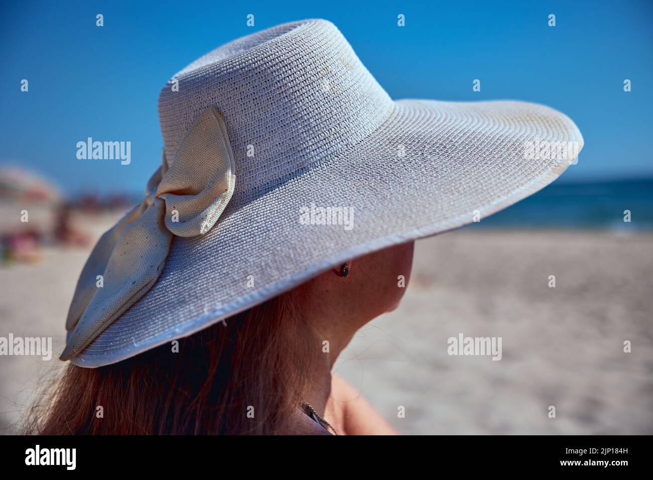 Adult mature woman in a white hat with large brim on the sea beach Stock Photo
