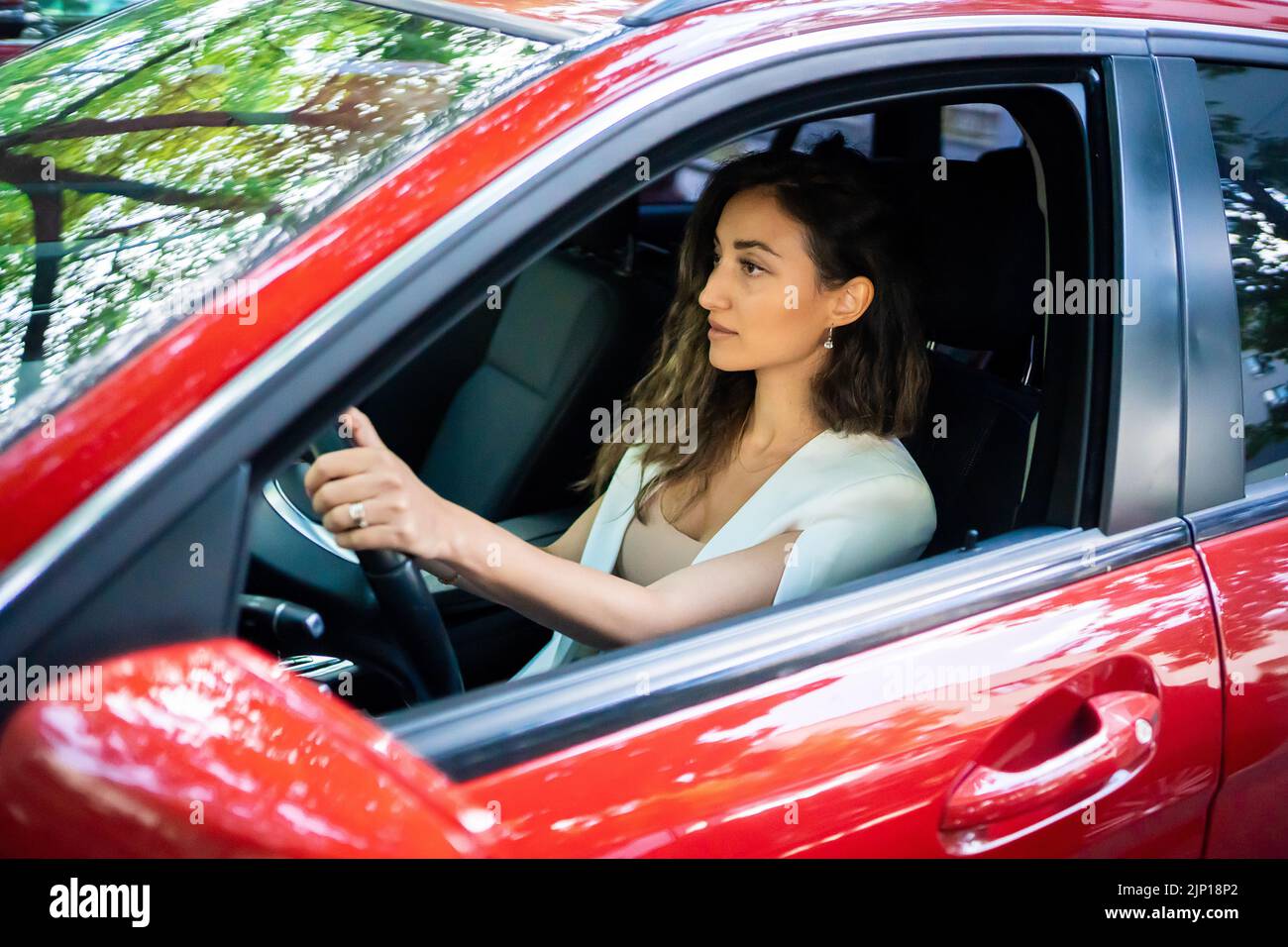 Happy smiling woman driver behind the wheel red car. View through car window Stock Photo
