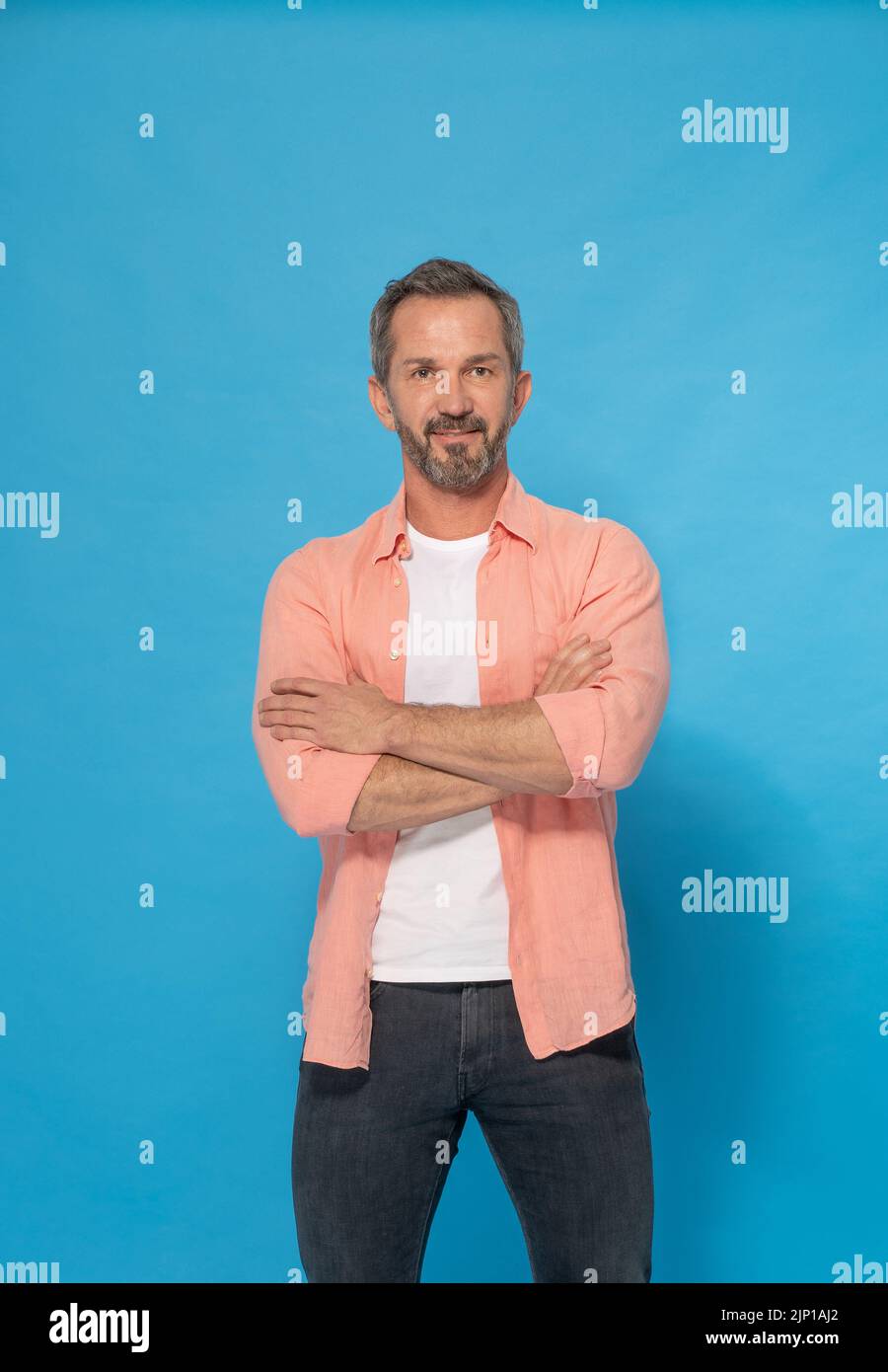 Strong handsome middle aged man with grey beard 40s, 50s wearing casual isolated on blue background. Smiling mature muscular, fit, athletic man posing in studio. Mature fit man health and physics.  Stock Photo