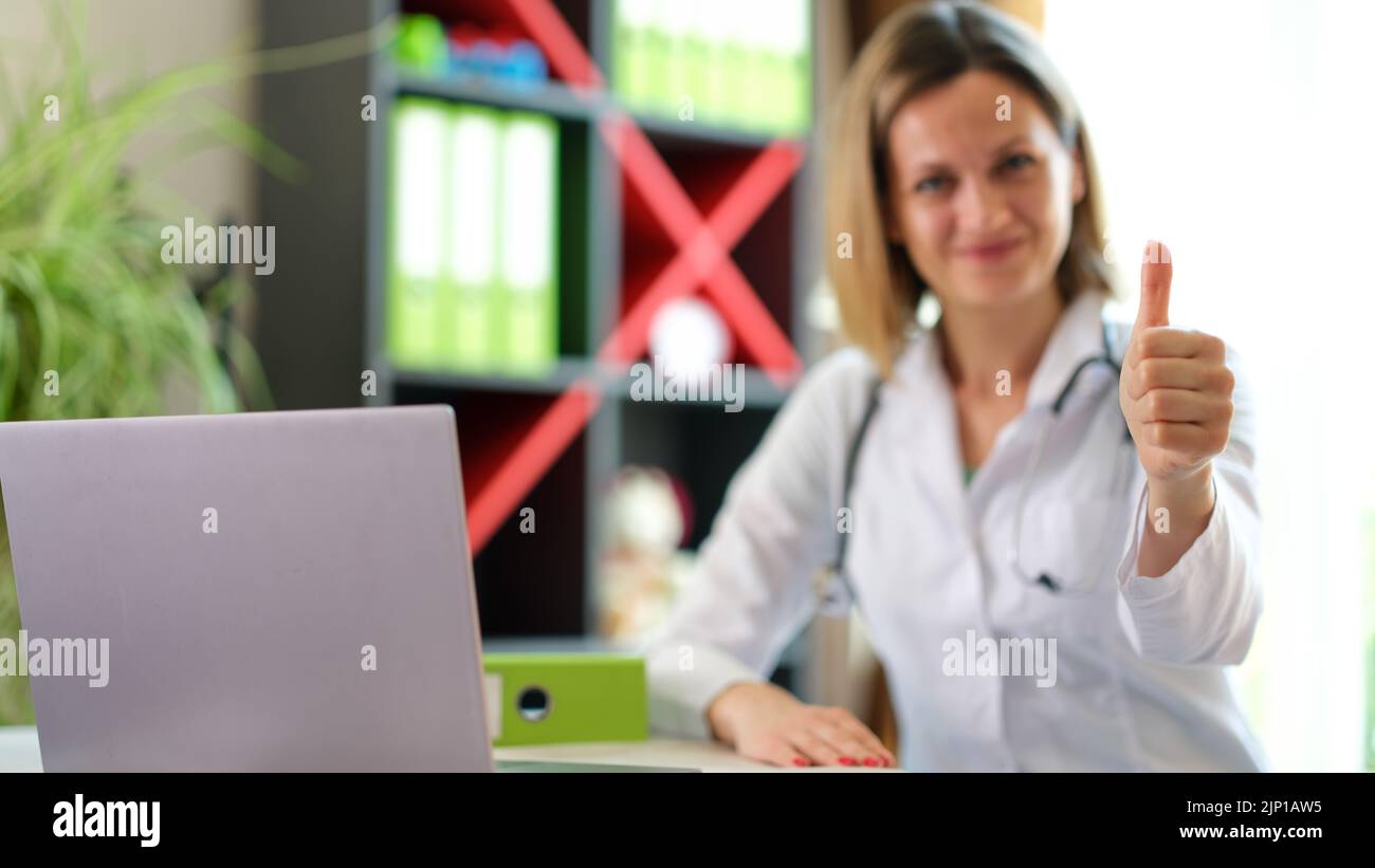 Smiling female doctor posing in clinic office and showing thumb up gesture Stock Photo