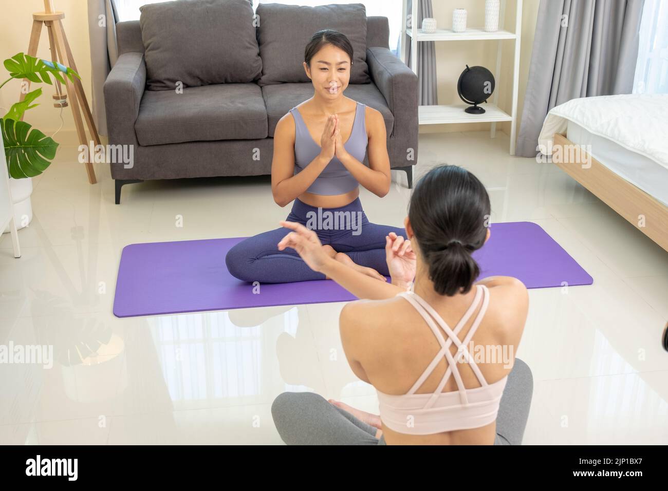 Asian people practicing yoga lifestyle class on a mat at living room. Young women with sports ware teach how to exercise yoga training at home Stock Photo