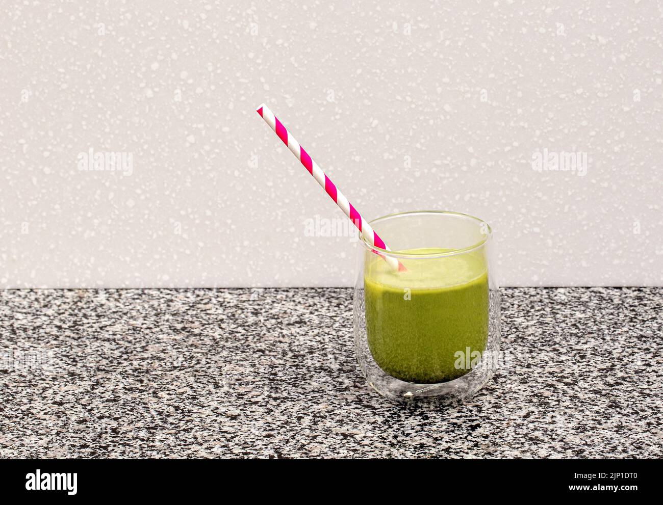Matcha tea in a glass cup with a red straw stands on a steel and in the