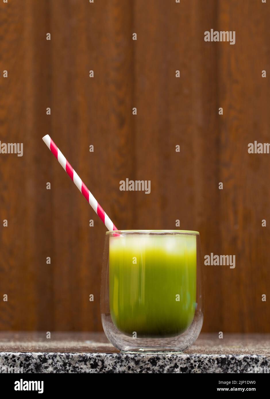 Matcha tea in a glass cup with a red straw stands on a steel and in the
