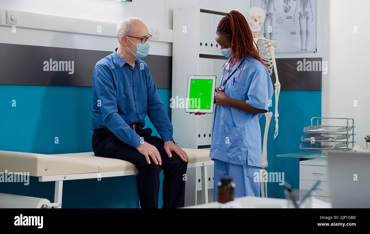 Woman and elderly man with face mask using greenscreen on tablet