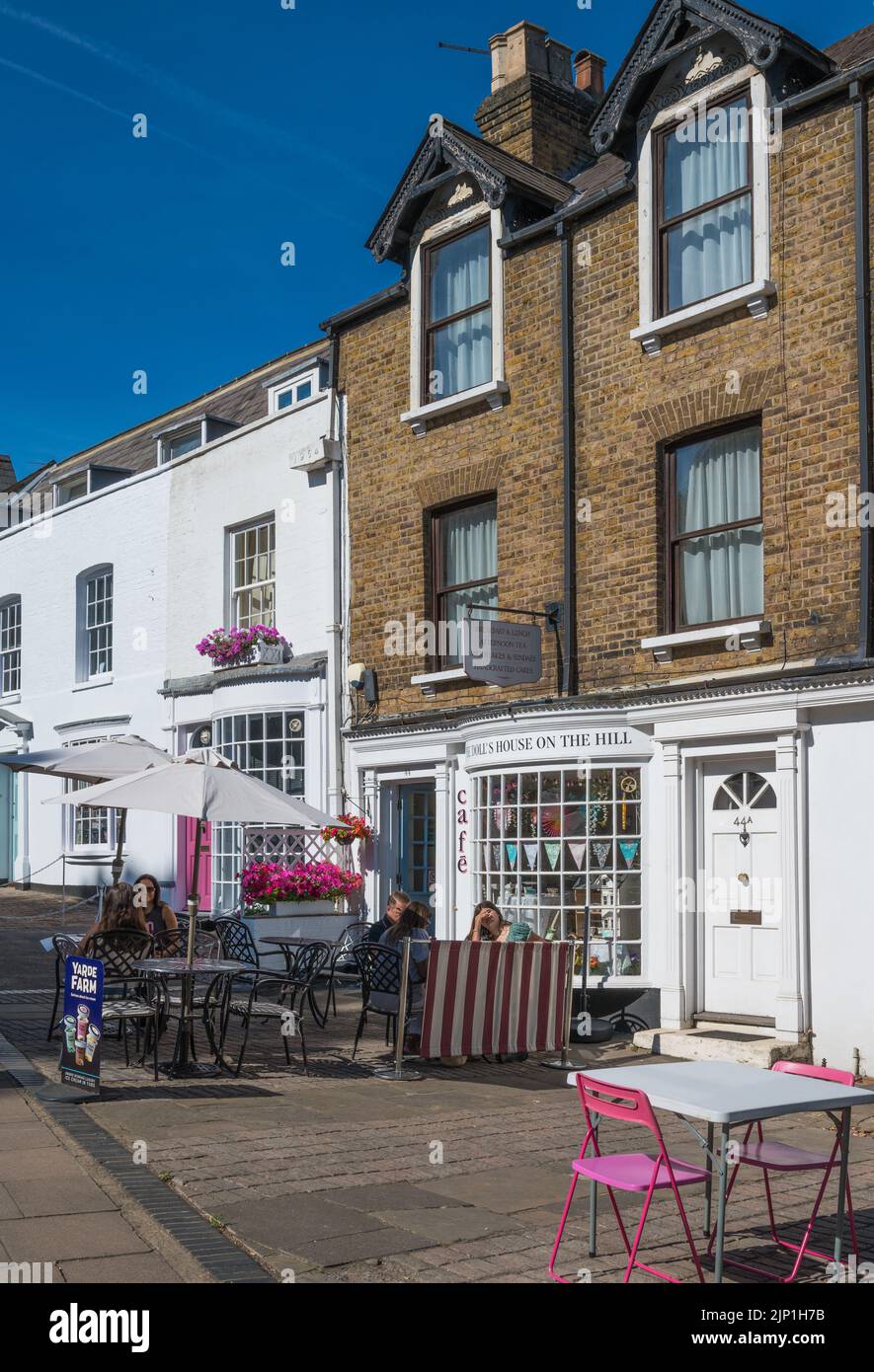 People seated at pavement tables on a sunny summer morning at The Dolls
