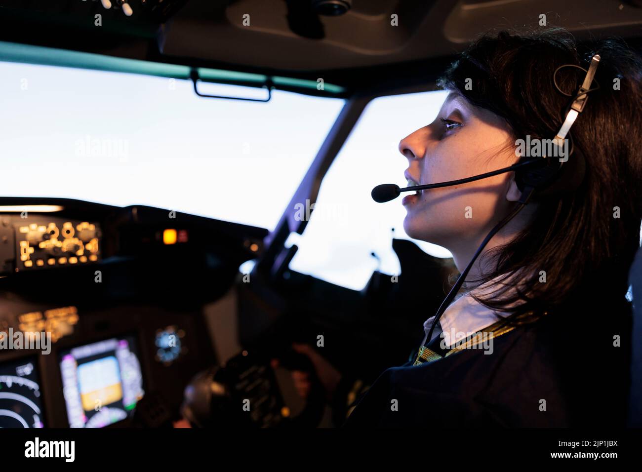 Female copilot flying plane from cockpit with dashboard command and control panel, using steering wheel and control panel for windscreen navigation. Woman using lever to fly aircraft. Stock Photo