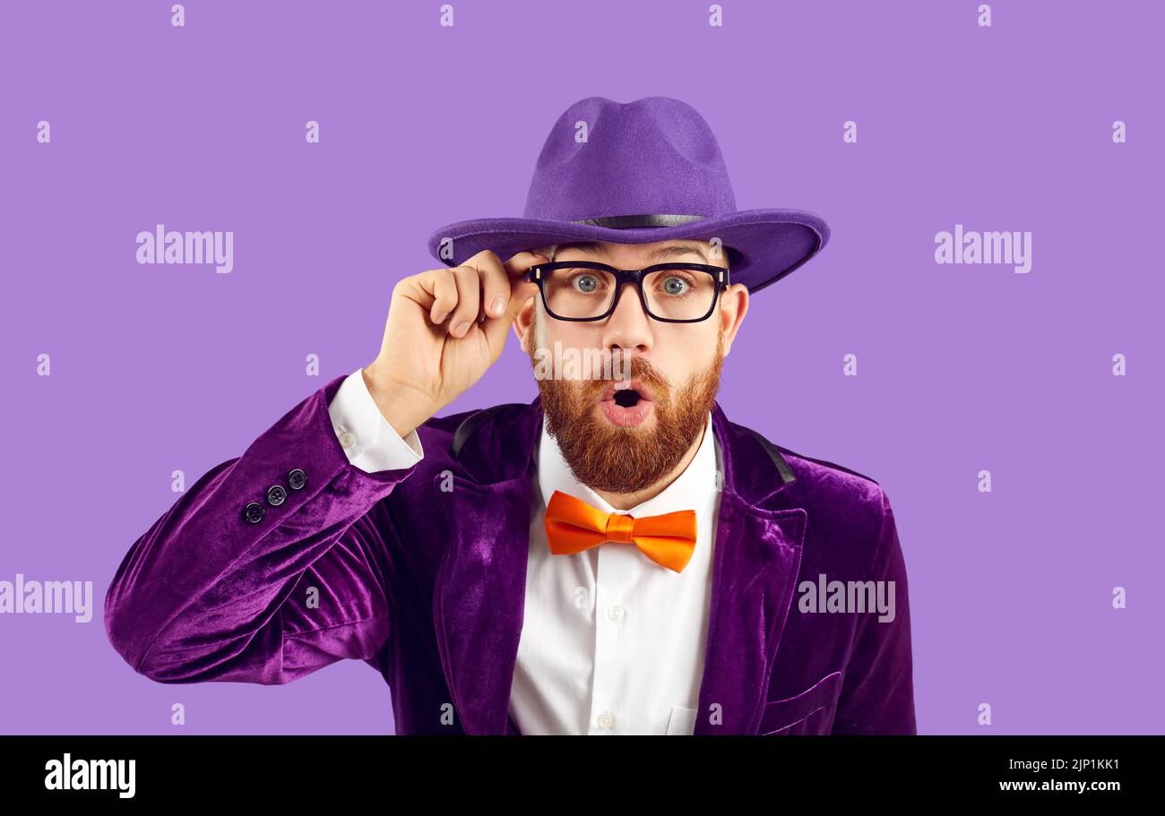 Stylish extravagant man looks at you with surprised and shocked expression on purple background. Stock Photo