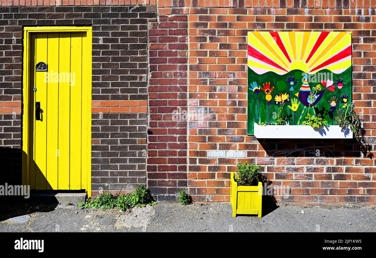 Happiness in a back lane with bright yellow door and painted flower boxes against a brick wall Stock Photo